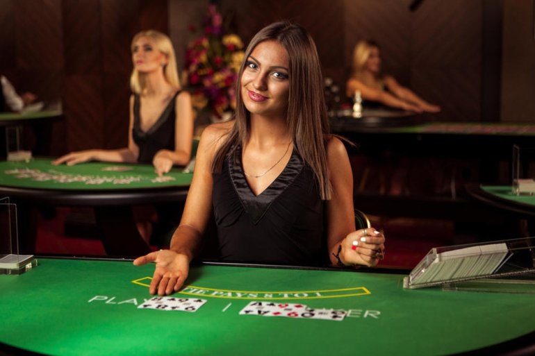 Симпатичная девушка крупье в черном платье с глубоким вырезом позирует за столом для баккара в ожидании игроков