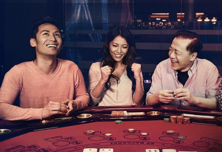 Азиатская красотка и двое мужчин азиатов хорошо проводят время за игрой в баккара в дорогом казино