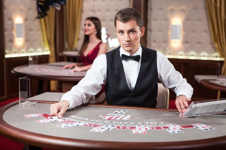 Молодой темноволосый парень крупье готов сыграть в блэкджек с клиентами казино