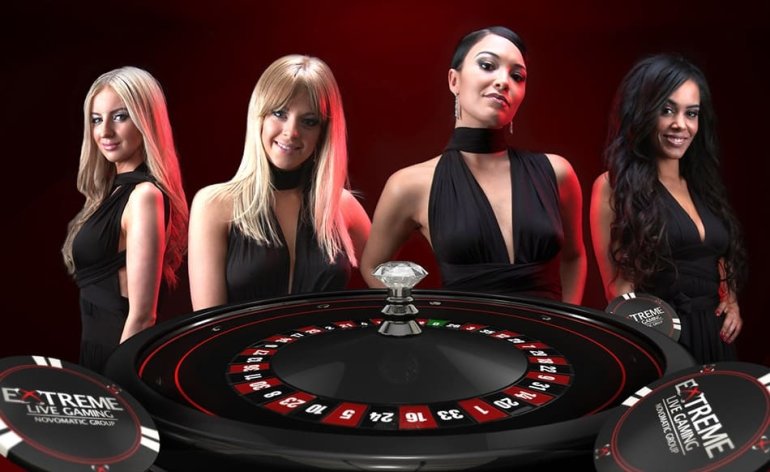 Четверо сексуальных девушек, блондинки, шатенка и темнокожая брюнетка, в черных обтягивающих платьях позируют у колеса рулетки