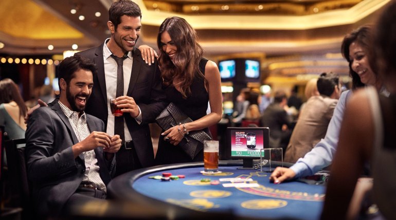 Красивая женщина в вечернем  платье и двое молодых мужчин в строгих костюмах за игрой в блэкджек в дорогом казино